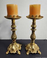 Two gold-tone metal candle holders with orange candles installed