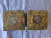 Two sealed boxes viewed from top with gold swirl design