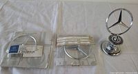 Three items displayed: standing hood ornament and two packaged emblem badges