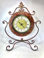 Front view of ornate metal clock showing dial and stand