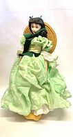Front view of porcelain doll in green dress and straw hat