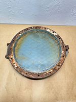 Front view of metal porthole window showing rusted frame and wire-reinforced glass