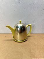 Front view of yellow Hall teapot with silver-tone cozy in place