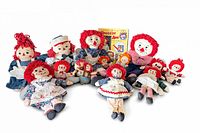 Group shot of fourteen Raggedy Ann and Raggedy Andy dolls with collector book