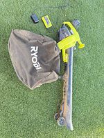 Full view of leaf vacuum/mulcher with collection bag, battery, charger and power adapter on turf