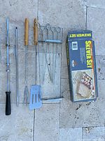 Entire lot laid out: rotisserie spit assembly, spatula, fork, skewer rack with 6 skewers, box