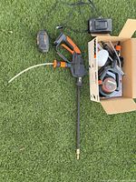 Full kit on grass showing sprayer, battery, charger and open box of accessories