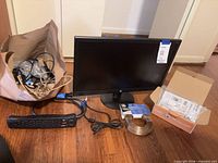 Front view of HP monitor, power strip, cable roll, Canon box, bag of cords