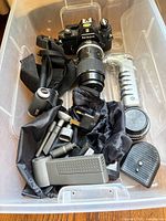 Overall lot in plastic bin showing Nikon camera with lens, monopod, binoculars and accessories