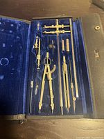 open case showing full set of brass drafting instruments in blue velvet