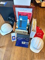 Group shot of lot showing hard hats, books, cap, headphones, framed certificate, file box