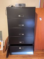 Front view of black filing cabinet with radio on top; one drawer open