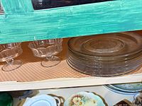 Stack of seven etched glass dessert plates and two footed bowls on shelf