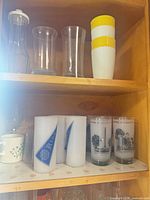 Shelf showing clear carafe, clear tumblers, plastic cup stack, printed frosted tumblers and ceramic mug