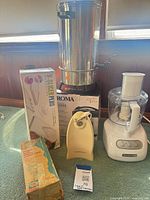 Group view: coffee urn, KitchenAid processor, can opener, Aroma rice cooker box, Börner mandoline box, Universal meat chopper box