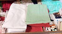 Drawer showing white towel, red placemats, green striped cloth, turquoise cloth, small boxes