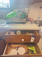 Countertop with KitchenAid dish rack filled with cups; open drawers showing flatware and trivets