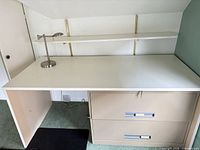Overall view of desk surface, lamp, shelf, portion of filing cabinet