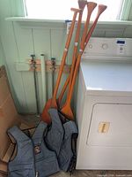Two blue Stearns vests and four wood paddles leaning beside dryer