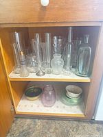Overall view of two shelves showing variety of glass vases and ceramic bowls