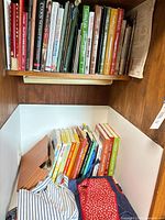 Two cabinet shelves showing large assortment of cookbooks and aprons at lower shelf