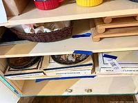 Cabinet shelf showing wicker basket with linens and two slatted wood shelves