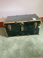 Front view of green metal trunk with brass hardware