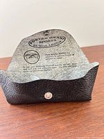 Interior view of black textured case showing Foster Grant Sports Sunglasses logo and snap closure