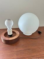 Lamp disassembled showing wood base with socket, frosted globe shade, bulb, cord with switch