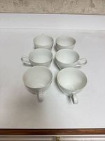 Six white porcelain teacups arranged on surface