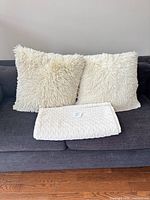 Two cream shag pillows on dark sofa with folded cream blanket