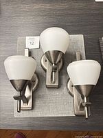 Three brushed nickel wall sconces with frosted glass shades displayed on tabletop