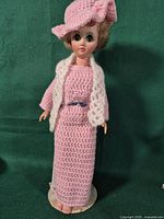 Full view of doll with crocheted dress, hat, scarf on stand