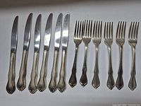 Five serrated knives next to six forks on flat surface