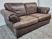 Front angle of brown leather two-seat sofa showing cushions, arms and wear