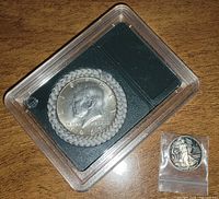 Kennedy half dollar in display holder alongside small silver round