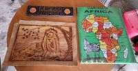 Three wall art pieces: cloth Africa map, banana-leaf lion on burlap, carved Karibu Welcome sign