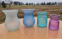 Four colored textured glass vases on table outdoors