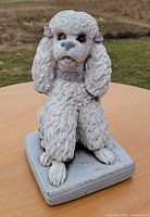 Front view of concrete poodle statue showing missing left glass eye and overall condition