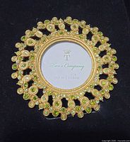 Front view of gold-tone round frame with green and clear rhinestones, Two's Company insert visible