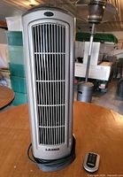 Front view of Lasko ceramic tower space heater showing grille and attached power cord with remote nearby