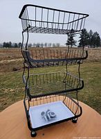 Full view of 4-tier black metal wire organizer rack, stationary feet visible, bag of wheels in bottom tray