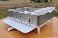 Side angle of Simplehuman dish rack showing stainless steel walls, white plastic base and drip tray