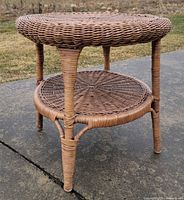 Side view of round wicker side table showing upper surface, lower shelf and leg structure