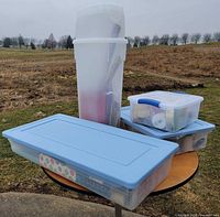 Two storage totes, cylindrical holder and latch-box shown outdoors