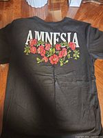Back of black T-shirt showing full AMNESIA text and floral graphic