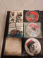 Open jewel cases showing Bon Jovi, Grease and Burton Cummings discs and inserts