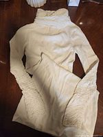 Full view of cream knit turtleneck dress with smocked cuffs laid flat
