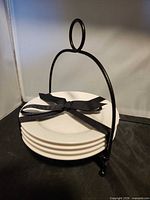 stack of four white plates tied with ribbon inside black metal stand
