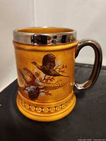 Full view of stein mug front showing glaze, pheasant motif, metal rim